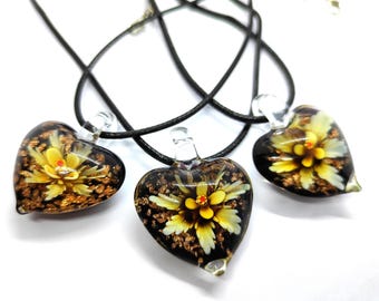 Puede incluir: Tres collares negros con colgantes de vidrio en forma de corazón. Cada colgante presenta una flor amarilla con detalles dorados sobre un fondo negro.