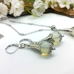 Puede incluir: Un collar de cadena de plata y pendientes a juego con un colgante de &oacute;palo en forma de l&aacute;grima. El colgante est&aacute; engastado en un dise&ntilde;o de flor de plata.