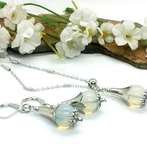 Puede incluir: Un collar y pendientes a juego de plata con un colgante de &oacute;palo blanco en forma de flor.