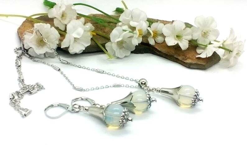 Puede incluir: Un collar y pendientes a juego de plata con un colgante de &oacute;palo blanco en forma de flor.