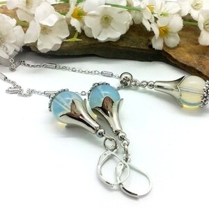 Puede incluir: Un conjunto de collar y pendientes de plata con un colgante de flor de &oacute;palo azul. El collar tiene una cadena delicada y los pendientes tienen un cierre de gancho.