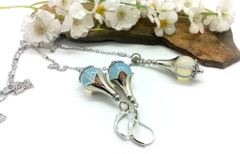 Puede incluir: Un conjunto de collar y pendientes de plata con un colgante de flor de &oacute;palo azul. El collar tiene una cadena delicada y los pendientes tienen un cierre de gancho.