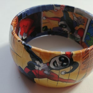 May include: A colorful bracelet made from comic book pages featuring Harley Quinn. The bracelet is yellow, red, black, and blue.