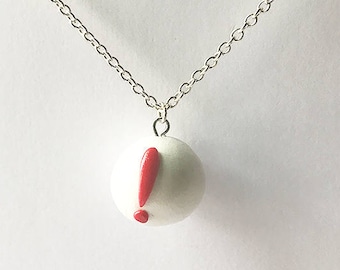 Op de afbeelding: Een zilveren ketting met een ronde witte hanger met een rood uitroepteken.