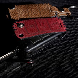 May include: A red and brown leather key fob with a silver key ring. The key fob has a black metal key attached to it.