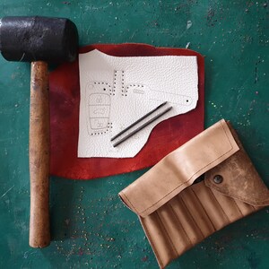 May include: A leatherworking kit with a hammer, two awls, a piece of leather with a pattern for a key fob, and a leather pouch with compartments.