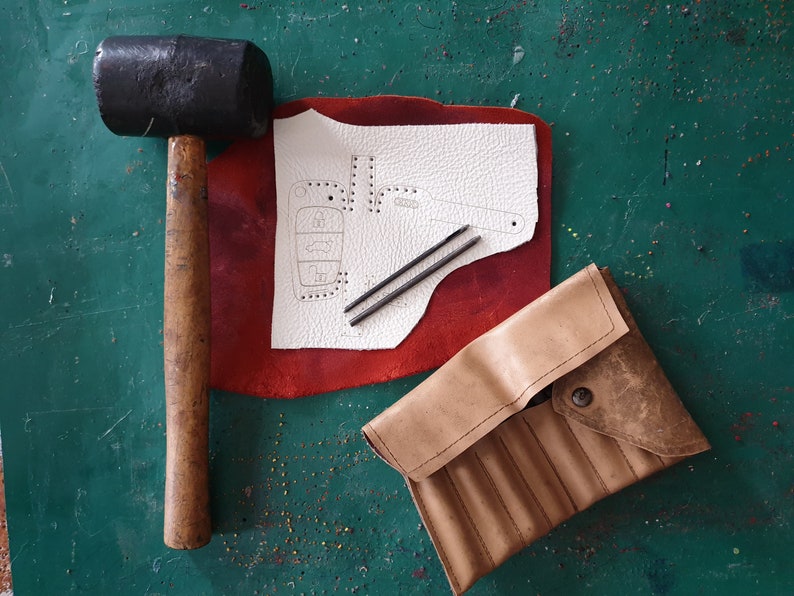 May include: A leatherworking kit with a hammer, two awls, a piece of leather with a pattern for a key fob, and a leather pouch with compartments.