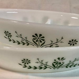 Puede incluir: Dos platos para hornear de cerámica blanca con un diseño floral verde. Los platos están apilados uno encima del otro.