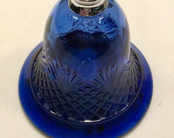 Puede incluir: Una campana de cristal azul cobalto con una parte superior de piña plateada. La campana tiene un patrón texturizado en forma de diamante en la base.