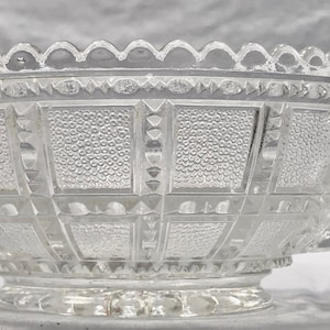 Może przedstawiać: Przezroczysta szklana miska z wyciętym wzorem. Miska ma uchwyt po jednej stronie i falisty brzeg.