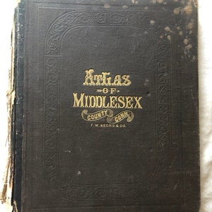 Può includere: Un libro nero con lettere dorate sulla copertina. Il titolo è "Atlas of Middlesex County Conn. F.W. Beers & Co."