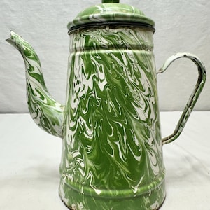 Könnte beinhalten: Vintage Kaffeekanne aus grün-weißem Emaille. Die Kanne hat ein wirbelndes Muster aus weißer und grüner Emaille. Sie hat einen Deckel, einen Ausguss und einen Griff. Ein klassischer Küchenartikel.