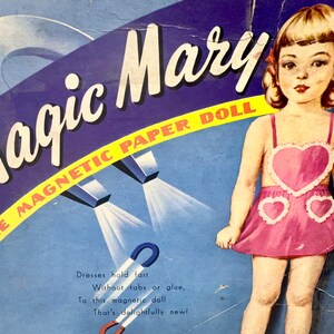 May include: A vintage box for a Magic Mary magnetic paper doll. The box features a colorful illustration of the doll wearing a pink dress with heart-shaped cutouts. The text on the box reads "Magic Mary The Magnetic Paper Doll" and "Dresses hold fast Without tabs or glue, To this magnetic doll That's delightfully new!"