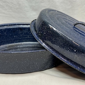 May include: Oval, dark blue enamel roasting pan with lid. The pan and lid have a speckled white pattern. The lid has a handle. The pan has two side handles. A kitchenware item for baking and roasting.