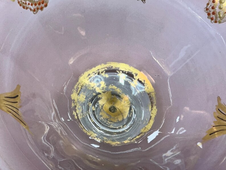 May include: A clear glass bowl with a decorative design. The bowl has a circular base with a yellow and gold rim. The bowl's interior features gold and yellow painted butterfly accents. The bowl has a light purple background.