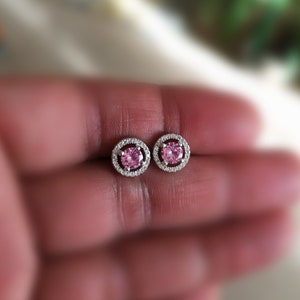 May include: A pair of silver earrings with a pink gemstone surrounded by a halo of smaller clear gemstones.