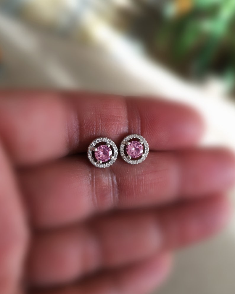 May include: A pair of silver earrings with a pink gemstone surrounded by a halo of smaller clear gemstones.