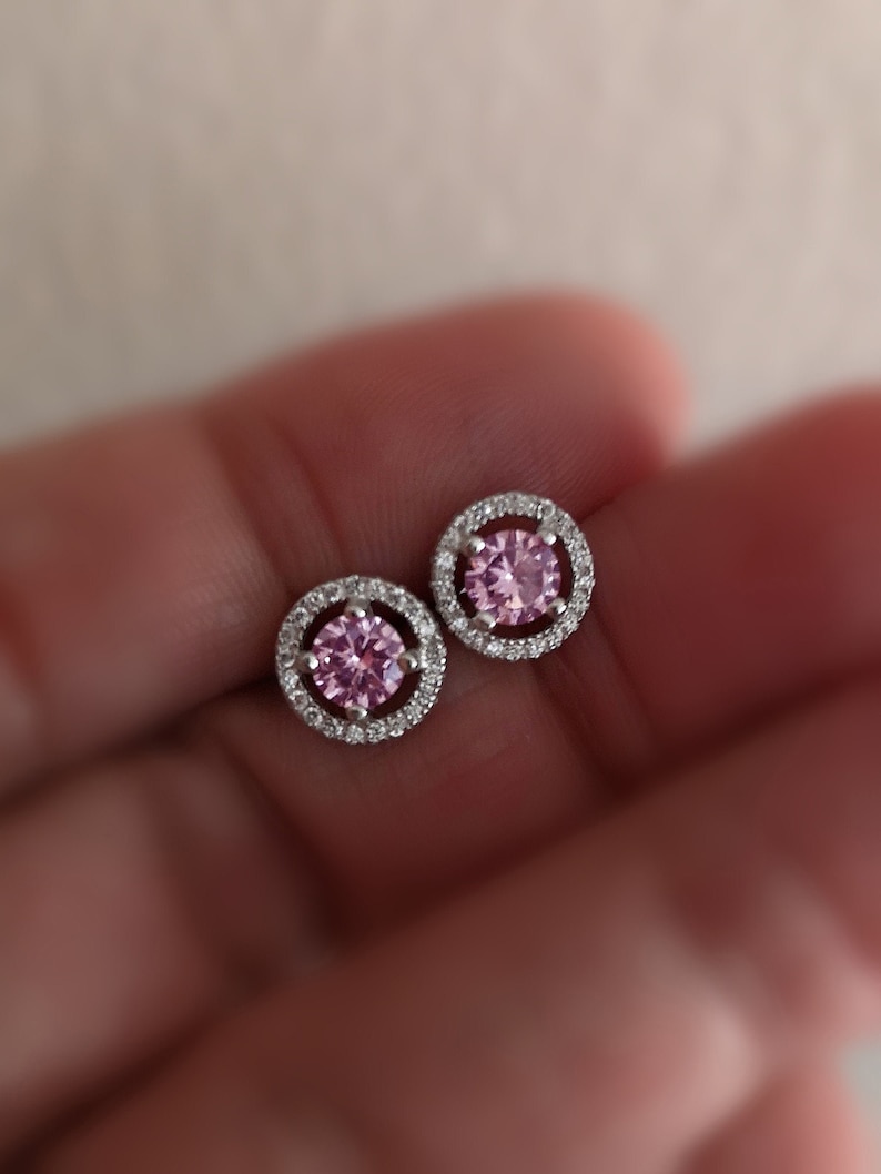 May include: A pair of silver stud earrings with a pink gemstone surrounded by a halo of smaller clear gemstones.