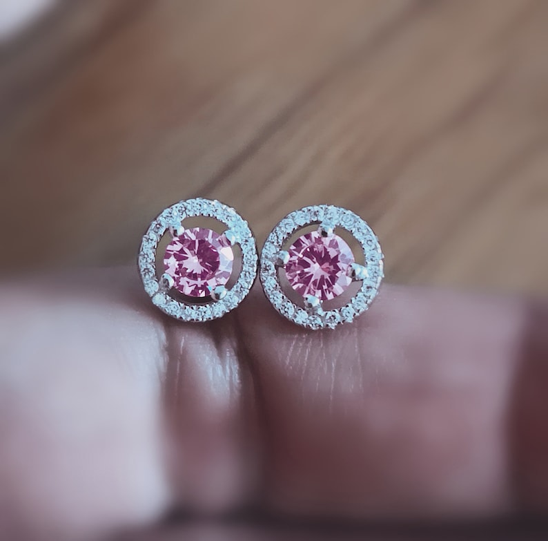 May include: A pair of silver earrings with a pink gemstone surrounded by a halo of smaller clear gemstones.