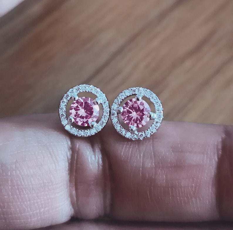 May include: A pair of silver earrings with a pink gemstone surrounded by smaller clear gemstones.