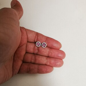 May include: A pair of silver stud earrings with a pink gemstone center and a halo of smaller white gemstones.