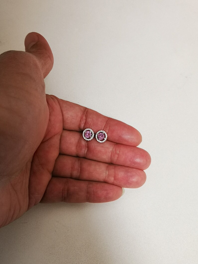 May include: A pair of silver stud earrings with a pink gemstone center and a halo of smaller white gemstones.
