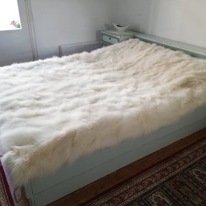 May include: A white faux fur throw blanket on a light blue bed frame. The blanket is soft and fluffy, and it would be perfect for adding a touch of luxury to any bedroom.