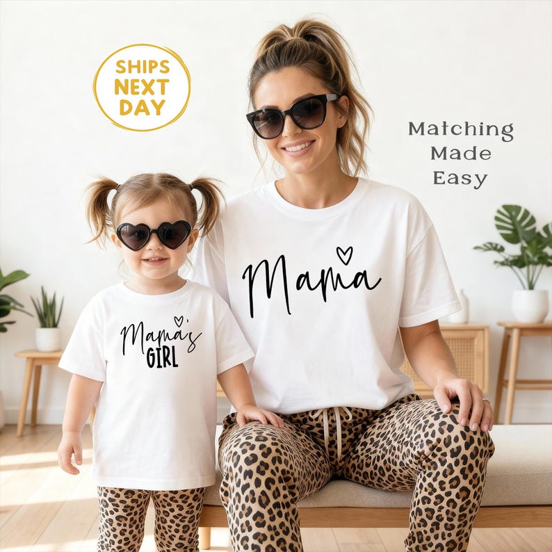May include: A woman and a child wearing matching white t-shirts with black script that reads "Mama" and "Mama's Girl". The woman wears sunglasses and leopard print pants. The child wears heart-shaped sunglasses and leopard print pants.