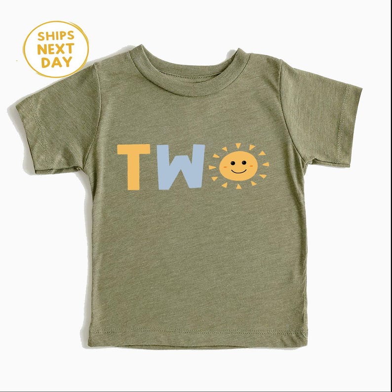 Puede incluir: Camiseta verde oliva para ni&ntilde;os peque&ntilde;os con la palabra "TWO" en amarillo y azul claro, y un gr&aacute;fico de sol sonriente. La camiseta tiene mangas cortas y cuello redondo. Un c&iacute;rculo amarillo con el texto "SHIPS NEXT DAY" est&aacute; en la esquina superior izquierda.