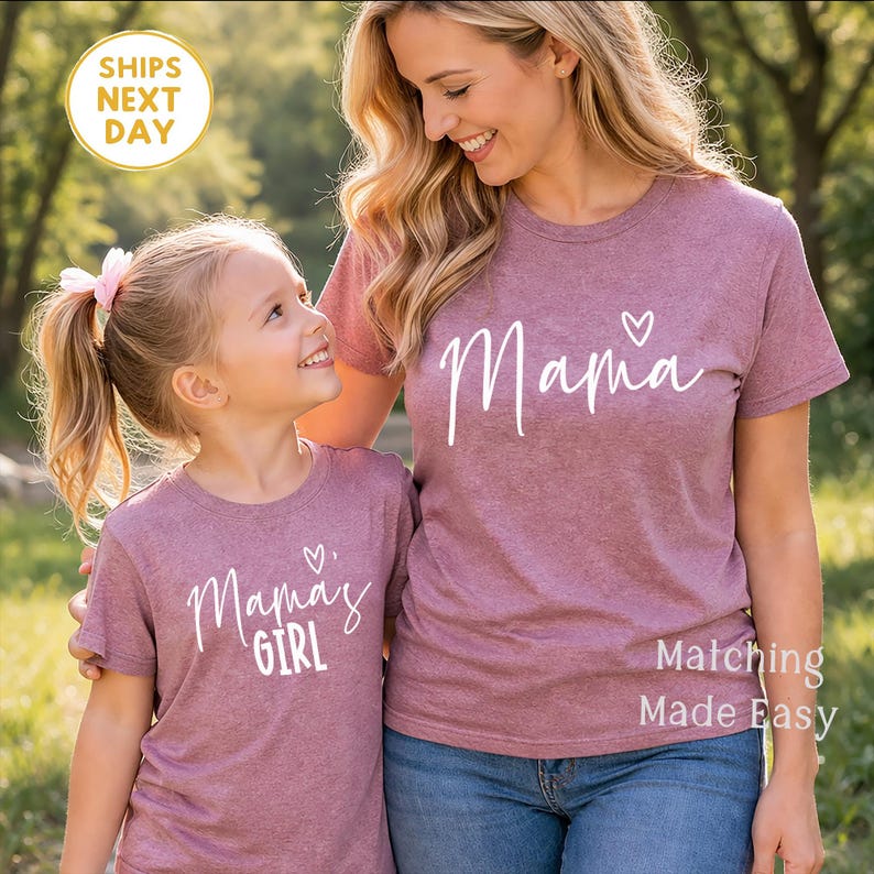 May include: Two matching mauve t-shirts, one for an adult and one for a child. The adult's shirt says "Mama" with a heart, and the child's says "Mama's Girl" with a heart. The image includes the text "Matching Made Easy".