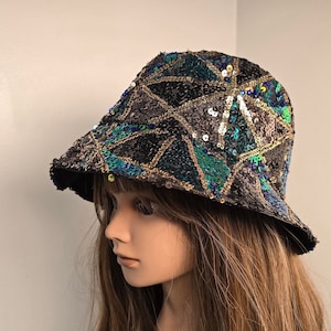 May include: A black bucket hat with a geometric pattern made of sequins in shades of green, gold, and blue.