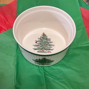 May include: A round white ceramic bowl with vertical ribbed sides and a green rim. The interior base features a detailed illustration of a decorated Christmas tree with gifts underneath, and a matching tree graphic is printed on the exterior side.