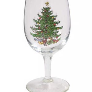 May include: A clear wine glass with a gold rim, featuring a festive Christmas tree design. The tree is green with colorful ornaments and a star on top, with wrapped gifts at the base. A holiday-themed glass for seasonal celebrations.