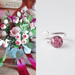 Peut inclure: Une bague en argent avec un délicat motif de feuille et un cabochon rond en résine transparente rempli de fleurs roses et blanches pressées.