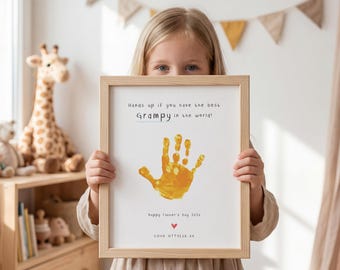 Puede incluir: Un marco con un marco de madera clara. La impresión presenta una huella de mano amarilla y el texto "Hands up if you have the best Grampy in the world!" y "Happy Father's Day 2006".