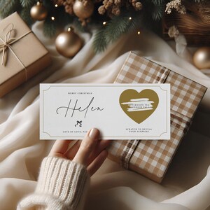 以下が含まれることがあります： 「Merry Christmas Helen」の文字とハート型のスクラッチエリアが付いたクリーム色のギフト券。 ギフト券は、包装されたギフトとクリスマスの飾り付けの近くにあり、お祝いの機会を示唆しています。