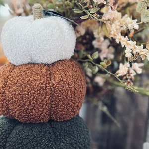 May include: A stack of three fluffy pumpkins in white, brown, and green. The pumpkins are made of a soft, fuzzy material and are perfect for autumn decor.