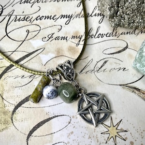 May include: A green cord necklace with a silver pentagram pendant, green and white beads, and a silver decorative clasp. The background features handwritten script and crystals.