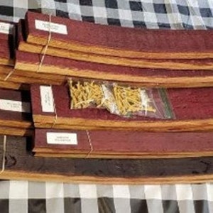 Puede incluir: Un conjunto de 15 duelas de barril de vino, algunas con una mancha marr&oacute;n rojiza, dispuestas en un patr&oacute;n escalonado. Las duelas est&aacute;n atadas con cuerda y hay peque&ntilde;os clavos dorados en el centro de la imagen.