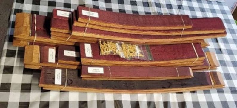 Puede incluir: Un conjunto de 15 duelas de barril de vino, algunas con una mancha marr&oacute;n rojiza, dispuestas en un patr&oacute;n escalonado. Las duelas est&aacute;n atadas con cuerda y hay peque&ntilde;os clavos dorados en el centro de la imagen.