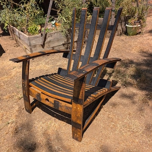 May include: A rustic outdoor chair constructed from reclaimed wood, with a curved back and armrests. The chair has a weathered appearance with dark and light brown tones. The chair is designed for comfort and relaxation, perfect for a garden.
