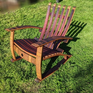 Puede incluir: Una mecedora de madera hecha de barriles de vino reutilizados. La silla tiene un acabado de madera natural y presenta un respaldo y un asiento de listones. La silla est&aacute; sentada en un c&eacute;sped verde.