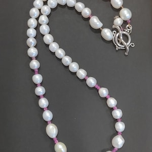 May include: A white pearl necklace with pink beads interspersed throughout. The necklace has a silver clasp.