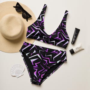 May include: A black bikini set with a geometric pattern in white and purple. The set includes a top and high-waisted bottoms. A straw hat, sunglasses, sunscreen, and a seashell are also in the image.