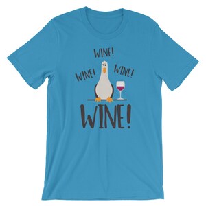 May include: A turquoise blue t-shirt featuring a cartoon seagull holding a glass of wine. The text "WINE!" is repeated four times on the shirt.