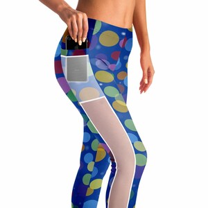 May include: Blue leggings with a colorful polka dot pattern and a mesh panel on the side. The leggings have a pocket on the side that can hold a phone.