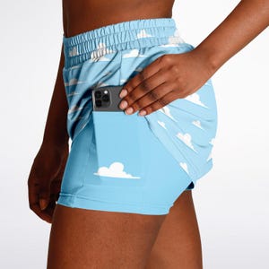 Peut inclure: Shorts de sport bleu clair avec un motif de nuages. Les shorts ont une poche intégrée contenant un smartphone. Les shorts ont un motif de nuages blancs et un fond bleu clair. La taille est élastique.