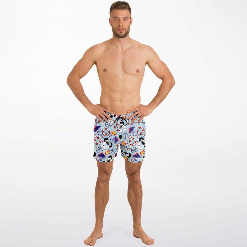 K&ouml;nnte beinhalten: Hellblaue Badeshorts mit nautischem Muster mit Ankern, Rettungsringen und Zeichentrickfiguren. Die Shorts haben einen Kordelzug in der Taille und ein farbenfrohes Design. Die Shorts sind knielang.