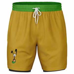 Puede incluir: Shorts deportivos amarillos con cintura verde y un gráfico de perro de dibujos animados en la pierna izquierda.
