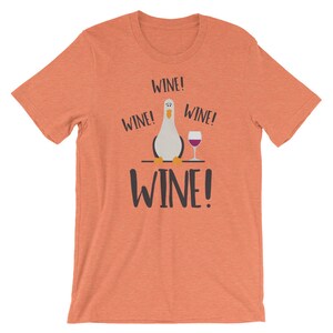 May include: A coral orange t-shirt featuring a cartoon seagull holding a glass of wine. The text "WINE!" is repeated four times on the shirt.